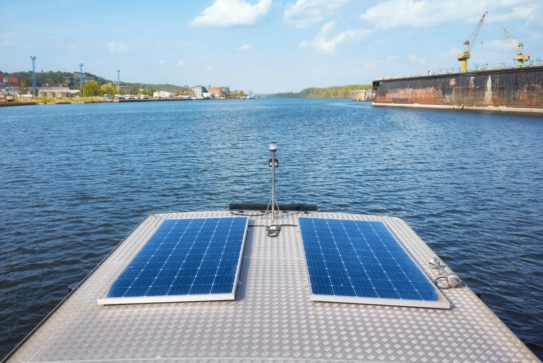 Solar panels mounted on the deck of a boat moored on a wide river.