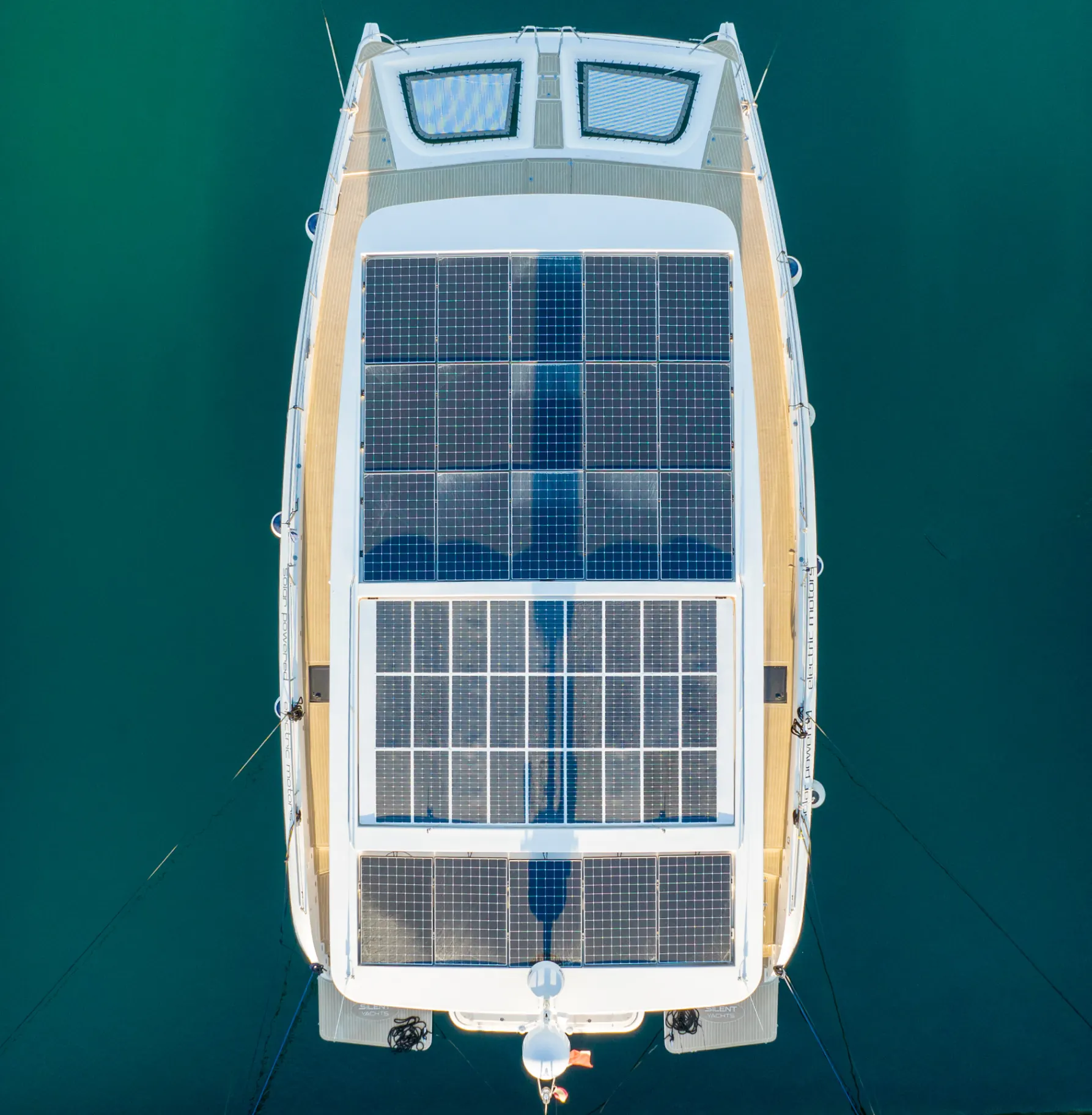 Aerial view of a catamaran with deck-mounted solar panels on turquoise water.